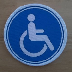 May include: A white accessibility symbol, showing a person in a wheelchair, is displayed on a blue circular patch with a white border.