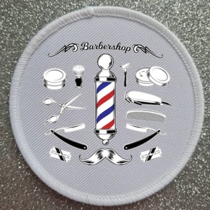 May include: A white round patch with a red, white, and blue barber pole in the center. The barber pole is surrounded by various barber tools, including scissors, razors, combs, and a shaving brush. The text "Barbershop" is written in a stylized font above the barber pole.