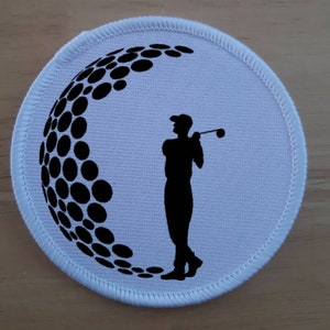 May include: White round patch with a black silhouette of a golfer swinging a club. A black and white golf ball design is in the background.