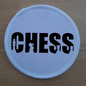 May include: White round fabric patch with black stitching around the edge. The word "CHESS" is printed in black with chess pieces incorporated into the letters.