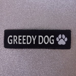 May include: Black fabric patch with white text that reads "GREEDY DOG" and a white paw print.