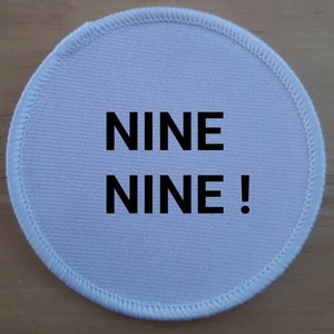 Può includere: Toppa rotonda in tessuto bianco con testo nero che dice "NINE NINE!"