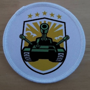 May include: A white round patch with a green tank with a yellow sunburst behind it. Five gold stars are above the tank.