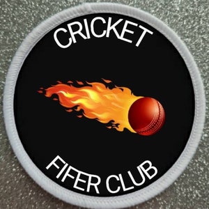 Può includere: Un cerotto rotondo bianco e nero con un bordo bianco. Il centro del cerotto presenta una palla da cricket rossa in fiamme con il testo "CRICKET FIFER CLUB" in bianco.