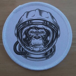 May include: A white round patch with a black and white illustration of a gorilla wearing an astronaut helmet.
