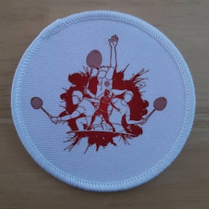 May include: White round patch with red embroidered design of four people playing badminton. The design features a red splatter background.