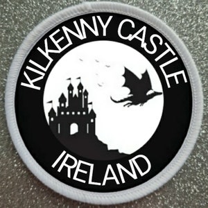 Puede incluir: Parche redondo blanco y negro con el texto "Kilkenny Castle Ireland" en un círculo blanco con una silueta negra de un castillo y un dragón volando.