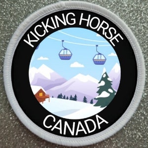 May include: A circular embroidered patch with a white border and a black frame featuring the text KICKING HORSE at the top and CANADA at the bottom. The centre depicts a snowy mountain landscape with a cabin, pine trees, and two ski gondolas.