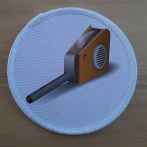 May include: A white round patch with a brown and black leaf blower design. The leaf blower has a black handle and a brown body with a white fan.