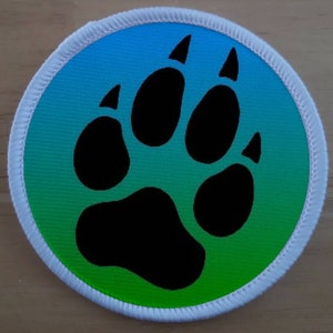 May include: A round, white patch with a green and blue gradient background. A black paw print is centred on the patch.