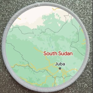 May include: A white circular patch with a green map of South Sudan. The map shows the country's borders and major cities. The text "South Sudan" and "Juba" are printed in red on the patch.