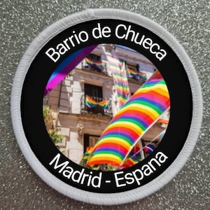 Könnte beinhalten: Ein runder weißer Patch mit schwarzem Text und einem Foto eines Gebäudes mit Regenbogenflaggen, die an den Balkonen hängen. Der Text lautet "Barrio de Chueca Madrid - Espana".