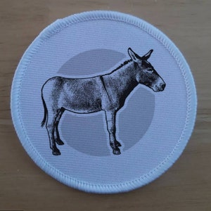May include: A white round patch with a black and white illustration of a donkey on a light gray background.
