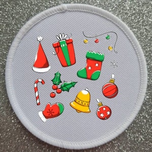 May include: A white round fabric patch with a colourful Christmas design. The design includes a Santa hat, a gift box, a stocking, a candy cane, a holly sprig, a bell, and baubles.