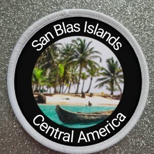 May include: A circular embroidered patch with a white border featuring a photographic print of a tropical beach with palm trees, turquoise water, and a wooden boat. The text San Blas Islands is at the top and Central America is at the bottom.