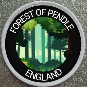 Op de afbeelding: Een witte ronde patch met zwarte tekst en een zwarte cirkel in het midden. De tekst luidt "FOREST OF PENDLE ENGLAND". De cirkel bevat een groene en blauwe illustratie van een bos.