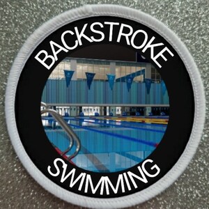 May include: A white and black circular patch with the words "Backstroke Swimming" in white text on a black background. The center of the patch features a photo of a swimming pool.