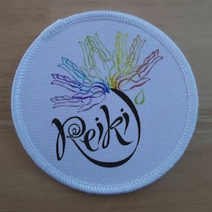 May include: White round fabric patch with a rainbow colored design of hands reaching up and the word "Reiki" in black cursive lettering.