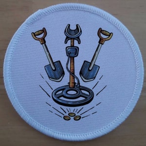 Pode incluir: Etiqueta redonda branca com um detector de metais, duas pás e moedas de ouro. O detector de metais é marrom com uma bobina preta. As pás são azuis com alças marrons. As moedas são de ouro.