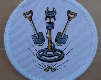 Könnte beinhalten: Weißer runder Patch mit einem Metalldetektor, zwei Schaufeln und Goldmünzen. Der Metalldetektor ist braun mit einer schwarzen Spule. Die Schaufeln sind blau mit braunen Griffen. Die Münzen sind aus Gold.