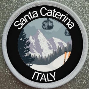 Pode incluir: Um remendo redondo branco com texto preto e um círculo preto no centro. O texto diz "Santa Caterina ITALY". O círculo contém um gráfico de uma cena de montanha nevada com um teleférico e esquiadores.