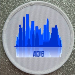 May include: White round fabric patch with a blue silhouette of the Vancouver skyline and the word "VANCOUVER" printed below.