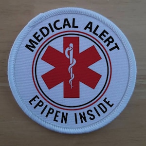 May include: White medical alert patch with a red star of life symbol and the text "MEDICAL ALERT EPIPEN INSIDE".