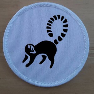 May include: White round fabric patch with a black silhouette of a lemur with a curled tail.