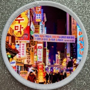 May include: A colourful image of a street in South Korea at night. The street is lined with shops and restaurants, and the buildings are decorated with neon signs. The signs are in Korean and English, and they advertise a variety of businesses, including restaurants, bars, and shops. The street is crowded with people, and the atmosphere is lively and vibrant.