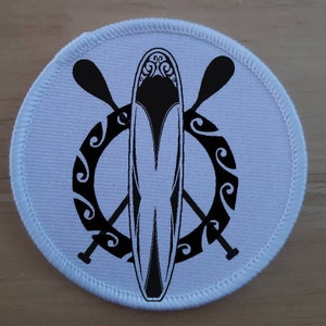 Pode incluir: Etiqueta redonda branca com uma ilustração em preto e branco de uma prancha de paddle e duas pás. A prancha de paddle tem um design decorativo na parte superior. As pás estão cruzadas atrás da prancha de paddle. O design é rodeado por um círculo preto e branco com um padrão decorativo.