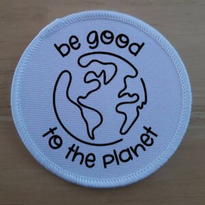 May include: White round patch with black stitching around the edge. The patch has a black outline of the Earth with the text "be good to the planet" around it.