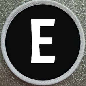 Peut inclure: Lettre E blanche sur un patch circulaire noir avec une bordure blanche.