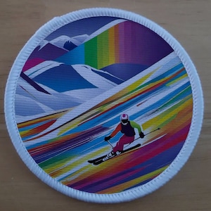 Pode incluir: Um remendo redondo colorido com um esquiador com um capacete branco e roupas vermelhas e pretas esquiando por uma montanha com um fundo de arco-íris.