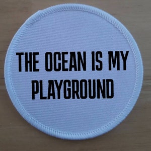 May include: White round patch with black text that reads "The Ocean is My Playground".