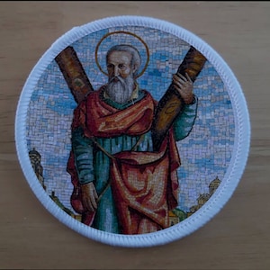 Könnte beinhalten: Ein runder, weißer Patch mit einem bunten Mosaikbild eines Heiligen, der ein Kreuz hält. Der Heilige trägt eine rote und blaue Robe und hat einen Heiligenschein über seinem Kopf.