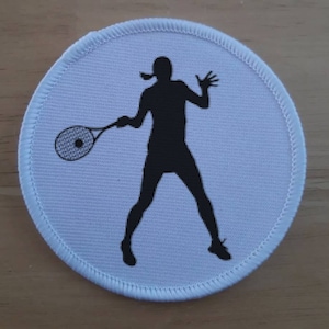 May include: White round patch with a black silhouette of a person playing tennis. The person is holding a tennis racket and is in mid-swing.
