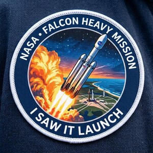 Puede incluir: Un parche bordado circular que muestra una escena de lanzamiento de cohete con una estela de fuego naranja brillante, un cielo azul y un paisaje costero. El texto NASA FALCON HEAVY MISSION e I SAW IT LAUNCH está impreso en blanco en el borde.