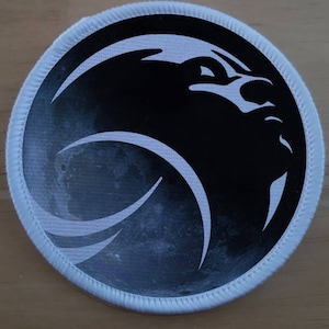 May include: A white circular patch with a black and white graphic of a stylized rocket ship with a moon-like background.
