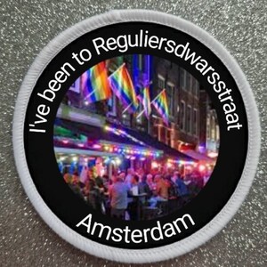 May include: A black and white round patch with the text "I've been to Reguliersdwarsstraat Amsterdam" around a colorful image of a street scene in Amsterdam.