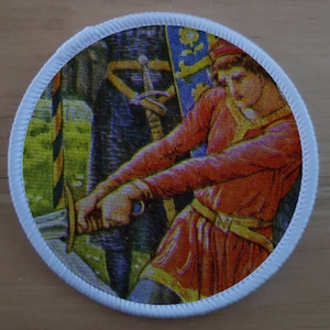 May include: A round white patch with a colorful image of a person in a red and yellow tunic holding a sword. The person is standing in front of a banner with a yellow and blue design.