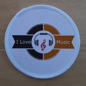 May include: White round patch with a black and gold circle design. The circle has a red treble clef and grey headphones. The text "I Love Music" is on a black and gold banner.