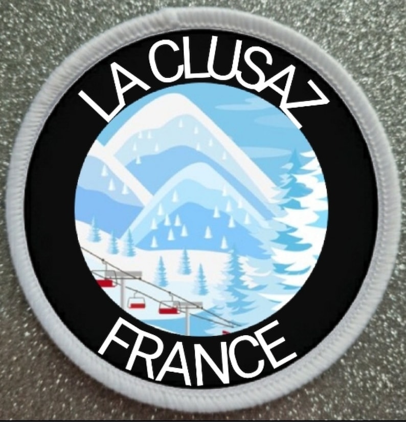 Puede incluir: Un parche redondo blanco y negro con un borde blanco. El centro del parche es negro con un gr&aacute;fico blanco de una cordillera con un remonte. El texto "LA CLUSAZ FRANCE" est&aacute; escrito en blanco alrededor del gr&aacute;fico.