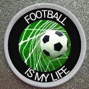 Könnte beinhalten: Runder weißer Patch mit schwarzem Rand und einem Fußball, der in ein grünes Netz geht. Der Text "FOOTBALL IS MY LIFE" ist um das Bild herum geschrieben.