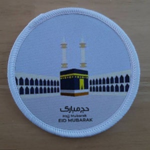 May include: White round patch with a blue and yellow illustration of the Kaaba, a cube-shaped building in Mecca, Saudi Arabia. The text "Eid Mubarak" is written in Arabic and English.