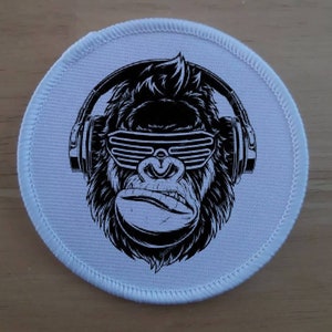 May include: A white round patch with a black and white illustration of a gorilla wearing headphones and sunglasses.