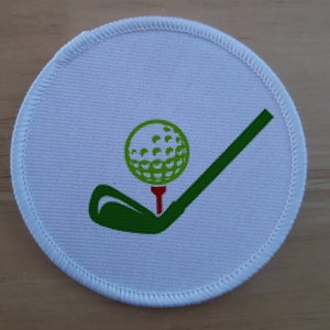 May include: White round fabric patch with a green golf club and a green golf ball on a red tee.