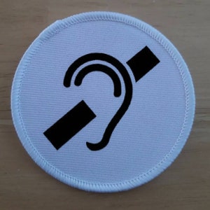 May include: White round patch with a black symbol of a hand over an ear with a diagonal line through it. The symbol represents hearing impairment.