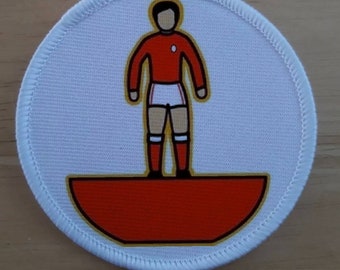 Könnte beinhalten: Ein runder weißer Aufnäher mit einem rot-weißen Fußballspieler, der auf einem roten und goldenen Halbkreis steht.