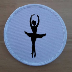 Könnte beinhalten: Runder Stoff-Patch in Weiß mit einer schwarzen Silhouette einer Ballerina in einem Tutu.