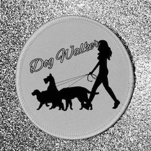 Peut inclure: Un patch rond blanc avec le texte "Dog Walker" en écriture cursive. Une silhouette d'une personne promenant trois chiens en laisse est représentée sous le texte.